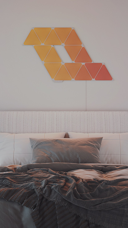 Esta es una imagen de un diseño de 15 paneles de Nanoleaf Shapes Triangles en la pared sobre la cama. Estos paneles de luz inteligentes son perfectos para iluminar la habitación y crear el ambiente ideal.