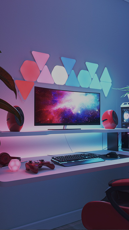 Esta es una imagen de los paneles de luz Nanoleaf Shapes en una sala de juegos. Son luces RGB perfectas para los jugadores en el entorno de tu hogar. Los paneles de luz modulares que cambian de color se conectan entre sí para crear un diseño con hexágonos y triángulos por encima del monitor.