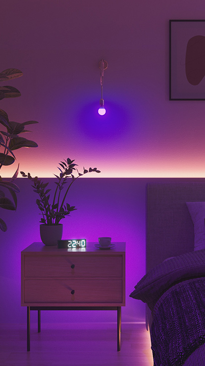 Esta es una imagen de una bombilla Nanoleaf Essentials en una habitación. La luminaria está en la pared entre la cama y la mesa de noche, lo que la convierte en la luz de dormitorio perfecta para crear el ambiente ideal.
