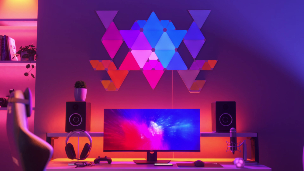 Esta es una imagen de Nanoleaf Shapes Triangles y Mini Triangles en la pared sobre el escritorio y detrás del monitor en una estación de batalla de juegos. Estas luces RGB tienen más de 16 millones de colores y son perfectas para el jugador de tu hogar. Los paneles de luz inteligentes modulares se conectan entre sí con conectores para crear un diseño.